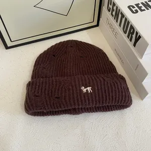 Close-up of dark brown distressed knit beanie featuring white animal embroidery detail