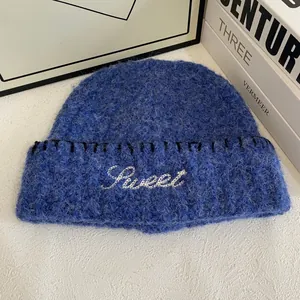 Detail of royal blue knit beanie featuring white Sweet embroidery and contrast stitching