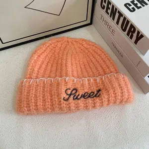 Detailed macro view of fuzzy orange-pink ribbed knit beanie with Sweet letter embroidery