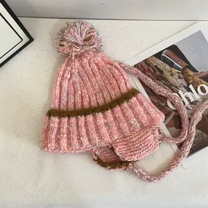 Detail of pink marled knit beanie with fluffy pom-pom and braided earflaps