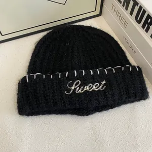 Detailed close-up of a black knit beanie featuring white 'Sweet' letter embroidery