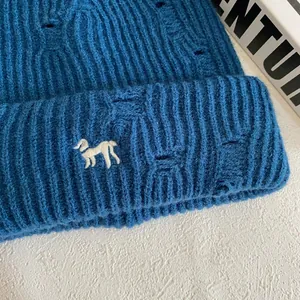 Detailed close-up of dark blue knit beanie with puppy embroidery and distressed ripped details