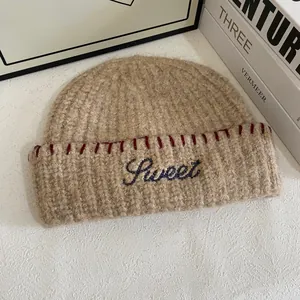 Detail of beige knit beanie showing blue Sweet embroidery and red contrast stitching
