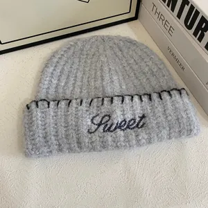 Detail of grey knit beanie featuring Sweet embroidery and black stitched edging finish