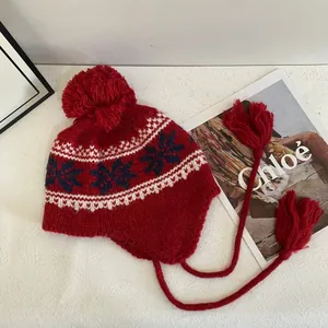 Close-up of red Fair Isle knit hat featuring winter snowflake patterns and plush pom-poms