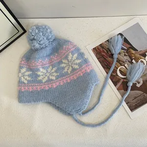 Detailed close-up of light blue knit hat featuring pink snowflake patterns and soft pom-poms