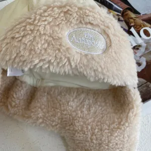 Macro detail of the plush faux shearling texture and embroidery on the beige earflap hat