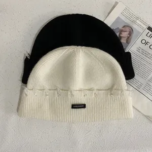 Gorros de punto minimalistas en negro y beige con detalles deshilachados y etiquetas tejidas