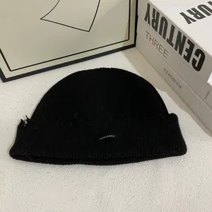 Detalle de los agujeros desgastados y el parche de marca en un gorro de punto negro