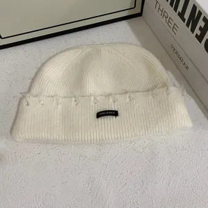 Textura detallada del gorro de punto acanalado blanco roto con etiqueta negra minimalista
