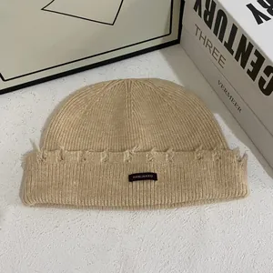 Vista de detalle del gorro de punto beige con etiqueta tejida y bordes deshilachados