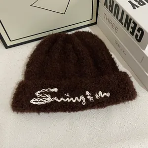 Detalle del gorro de punto de felpa marrón oscuro con bordado Sunrise blanco y textura suave