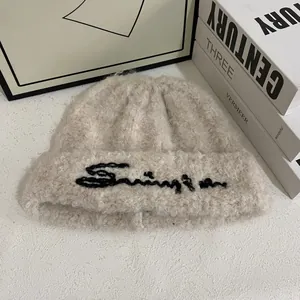 Detalle del gorro de punto beige tipo sherpa con bordado de letras y textura muy suave