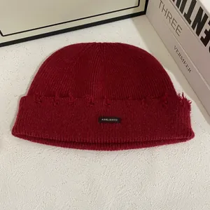 Detalle del gorro de punto burdeos con borde deshilachado y etiqueta de marca tejida