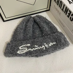 Detalle macro del gorro sherpa gris oscuro con bordado Swing blanco y textura rizada