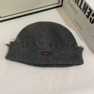Detalle de gorro de punto gris oscuro con bordes deshilachados y etiqueta de tela roja