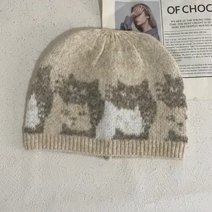 Detail of oat beige knit beanie featuring brown cat jacquard and ribbed cuff texture