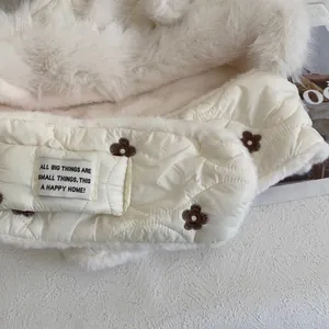 Close-up of beige quilted down neck warmer with plush fur lining and flower embroidery
