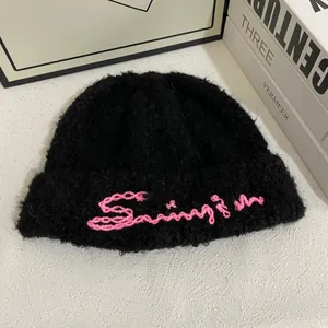 Primer plano del gorro de punto negro con bordado de letras rosas y textura gruesa