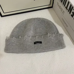 Detalle del gorro de punto acanalado gris claro con borde deshilachado y etiqueta negra