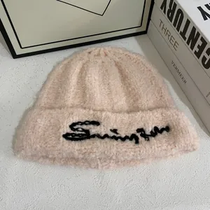 Detalle del gorro de punto rosa suave con bordado negro y textura de lana rizada