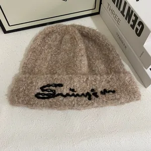 Primer plano de un gorro de punto de felpa marrón con bordado negro en fondo blanco