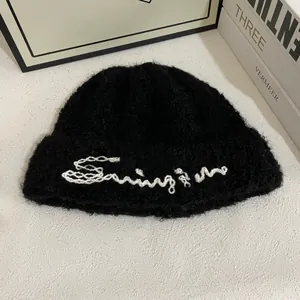 Detalle de gorro de punto de mohair negro con bordado de letra cursiva blanca