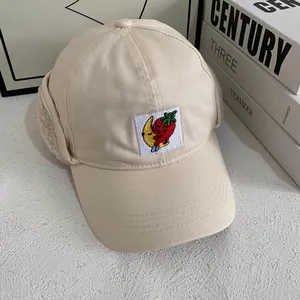 Detail of beige winter baseball hat with fleece earflaps and cute strawberry embroidery