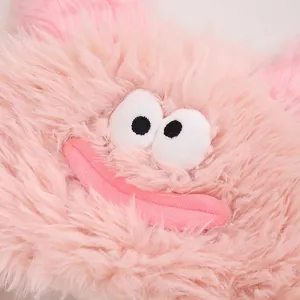 Détail du bonnet pelucheux rose avec grands yeux de dessin animé et bouche brodée