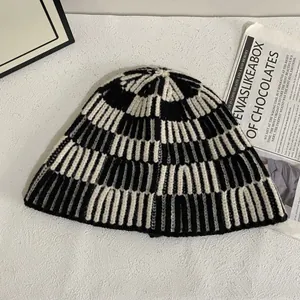 Chic black and white striped knitted bucket hat for women on white textured surface