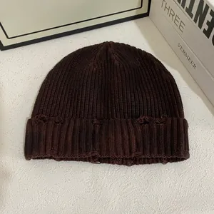 Gros plan sur un bonnet en tricot marron foncé avec des détails de trous déchirés