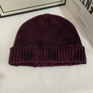 Détail macro du bonnet en maille bordeaux avec texture vieillie et déchirures