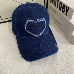 Detail of blue denim baseball cap featuring heart embroidery and distressed vintage texture