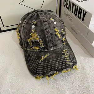 Close-up of distressed denim baseball cap with yellow frayed details and vintage wash effect