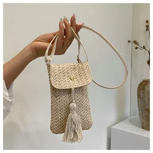 Detail of cream straw woven phone bag featuring a gold magnetic clasp and fringe tassel