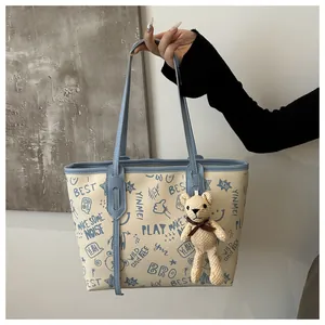 Dettaglio borsa tote in PU crema con graffiti blu e ciondolo a forma di orsetto peluche