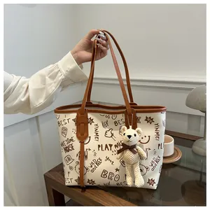 Dettaglio della borsa tote bianca con graffiti, manici marroni e ciondolo a forma di orso