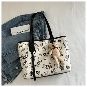 Dettaglio della borsa tote in PU bianco con graffiti neri e ciondolo a forma di orso