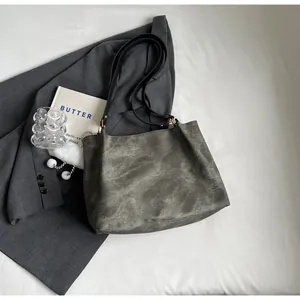 Détail du sac cabas gris texturé avec lanières en cuir noir et pompon blanc décoratif