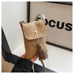 Close-up of handmade straw woven phone bag featuring tassel detail and gold buckle