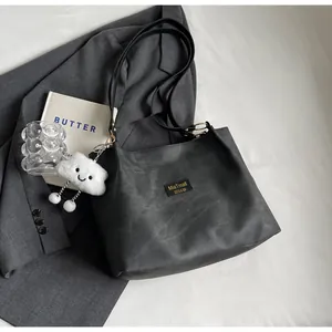 Détail d'un sac cabas noir mat avec étiquette tissée et joli pendentif nuage en peluche