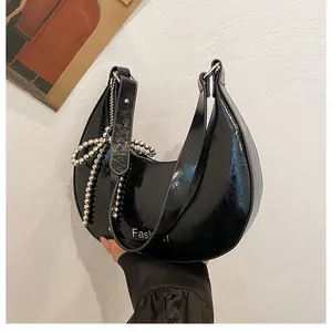 Close-up of black glossy patent leather shoulder bag with silver beaded bow detail