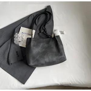 Détail du sac fourre-tout gris foncé avec texture vintage et breloque pompon blanc