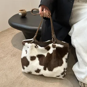 Dettaglio della borsa tote in peluche con stampa mucca e manici in pelle marrone scuro
