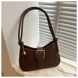 Détail du sac demi-lune marron foncé avec boucle dorée sur fond de tricot blanc cassé