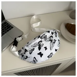 Elegante borsa a tracolla bianca con stampa a farfalla e cinturino su una scrivania moderna