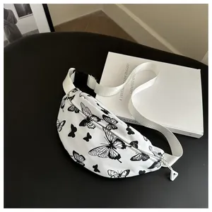 Dettaglio del marsupio in tela bianca con motivi a farfalla neri e tracolla regolabile