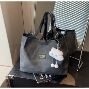 Détail du sac cabas en cuir gris foncé avec écusson logo et breloque nuage en peluche