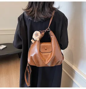 Detail of a brown vintage PU leather tote with a plush lion charm on a black coat