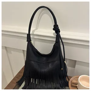 Detalle de bolso de hombro negro con textura de lichi, flecos largos y nudo decorativo